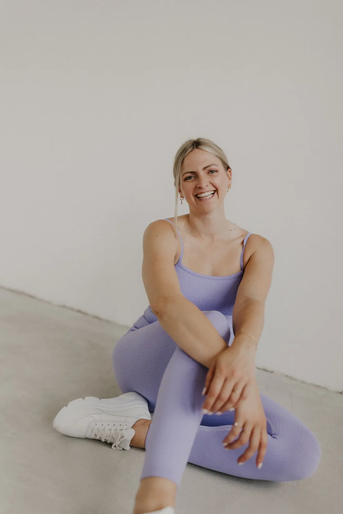 Sabrina sitzt lachend auf dem Boden, in lila Sportoutfit